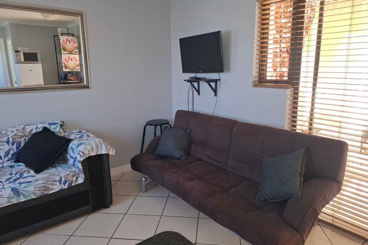 A living room area featuring tiled flooring, neutral wall paint, and a window fitted with wooden blinds.