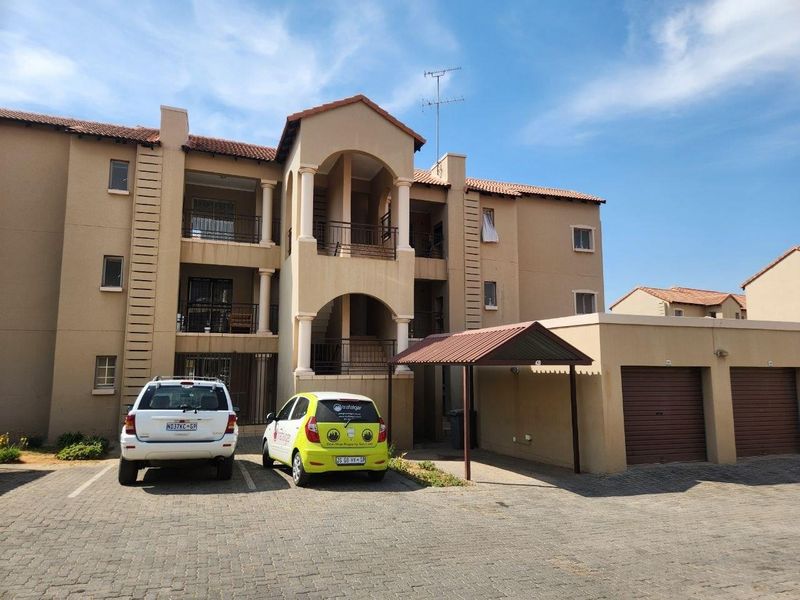 Front elevation of a multi-story apartment complex featuring balconies, a covered carport, and private garage units with paved driveway access.
