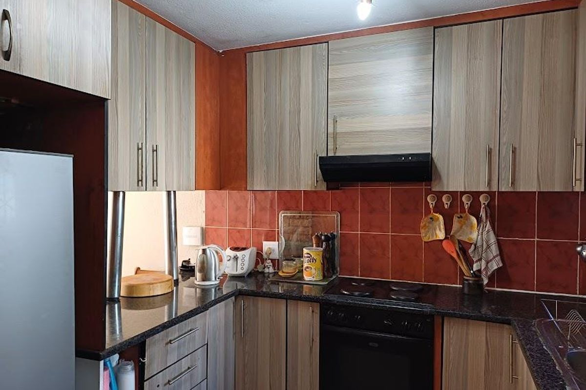 A functional kitchen featuring wood-look laminate cabinetry, granite countertops, a tiled backsplash, and integrated cooking appliances including an oven and extractor fan.