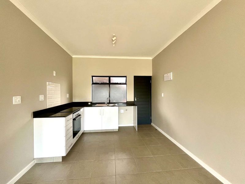 A clean, modern kitchen featuring white cabinetry, dark countertops, built-in oven, and tiled flooring in an open-plan layout.