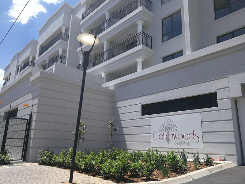 Exterior view of the Cottonwoods apartment complex entrance, featuring modern architectural design, balconies with railings, and well-maintained landscaping.