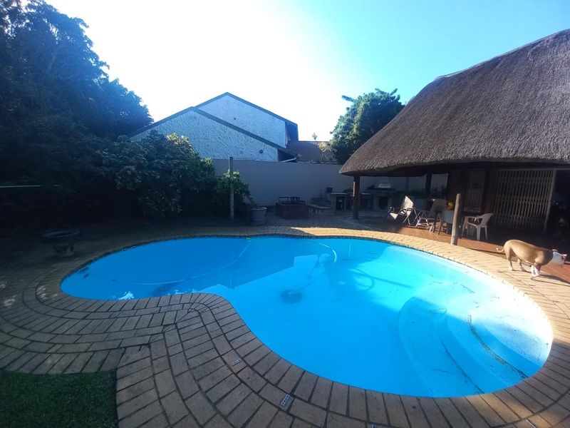 Outdoor entertainment area featuring a swimming pool and a thatched roof lapa with a built-in braai, set within a private garden.