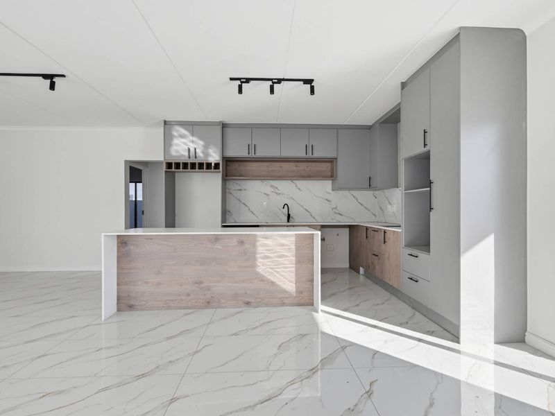 Modern open-plan kitchen featuring sleek grey and wood-tone cabinetry, marble-look tiled flooring, a central island, and contemporary track lighting.