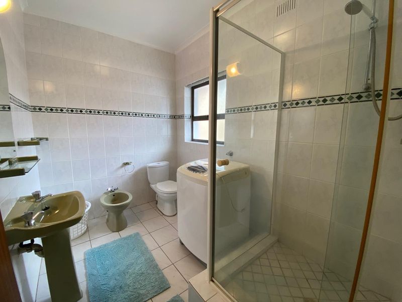 A functional bathroom featuring a pedestal basin, bidet, toilet, and a glass-enclosed shower with tiled finishes throughout.