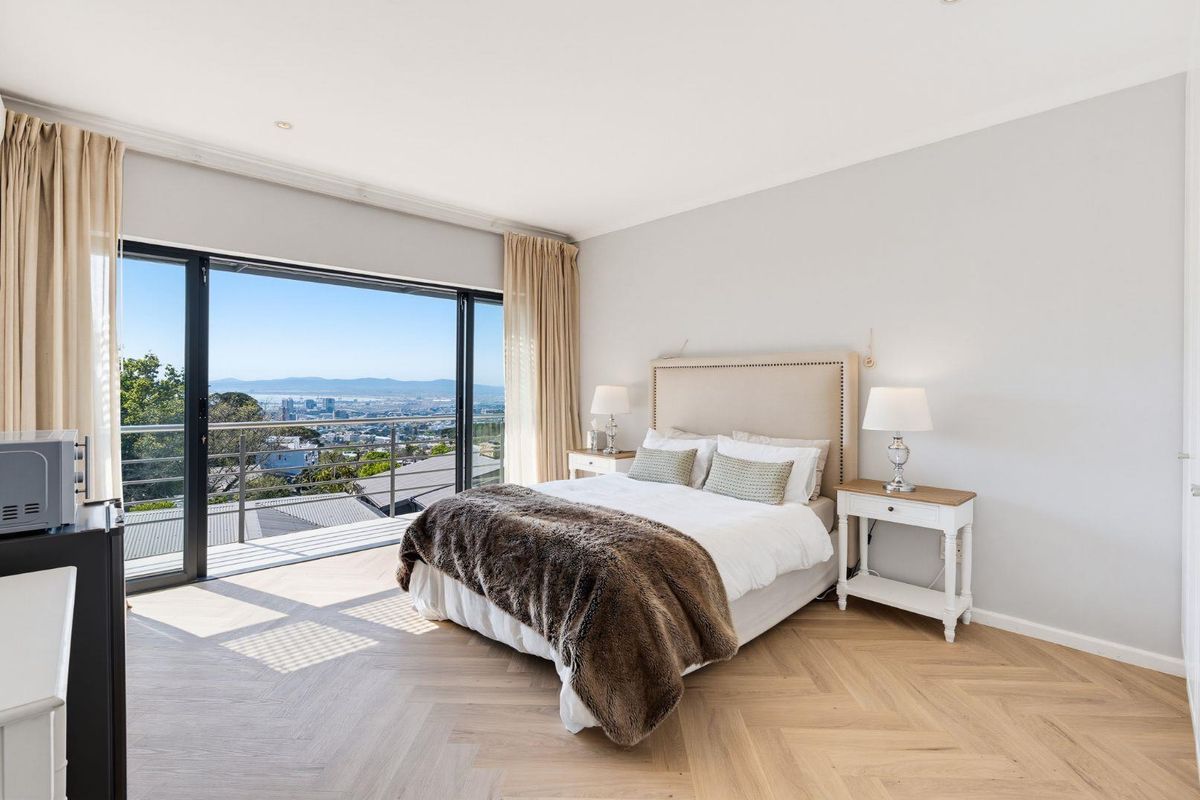 A bright, modern bedroom featuring elegant herringbone timber flooring and large sliding glass doors that open to a balcony with expansive city views.
