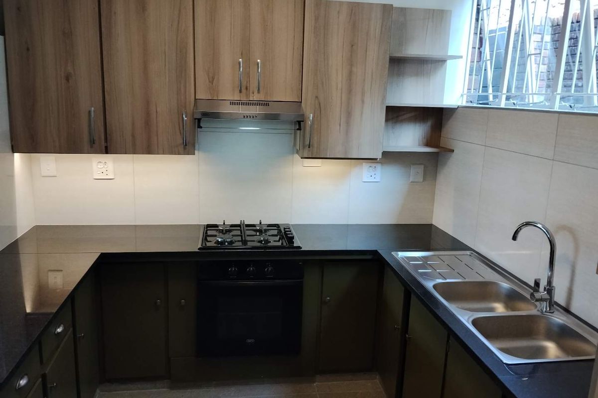 A modern, well-maintained kitchen featuring wood-finish cabinetry, granite countertops, a gas hob, built-in oven, and a double stainless steel sink.