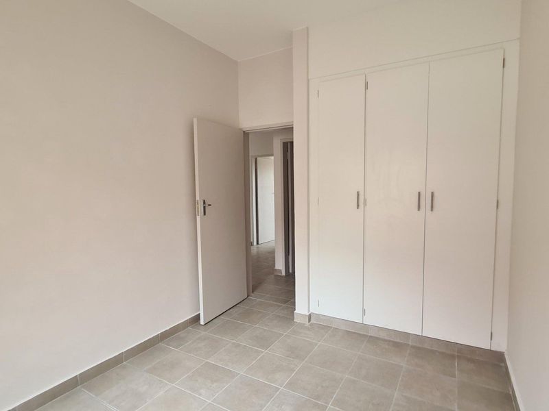 A clean, empty bedroom featuring neutral tiled flooring and built-in white cupboards, offering a blank canvas for personalization.