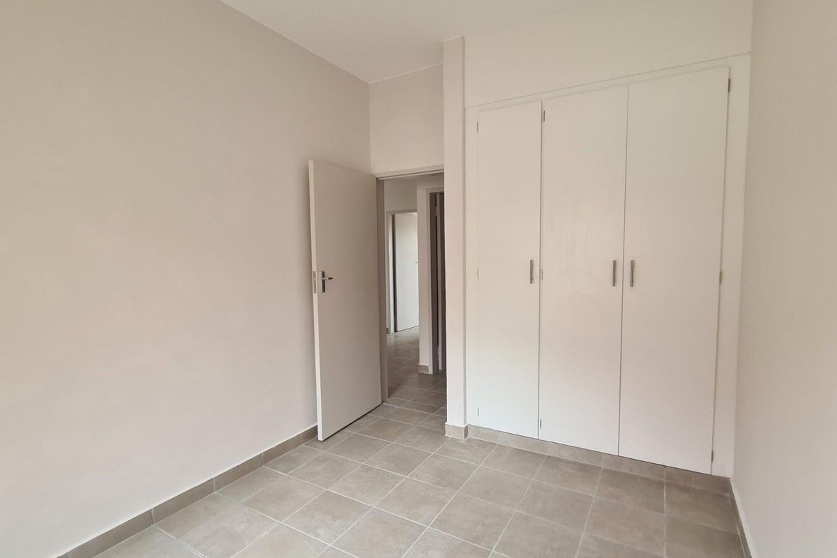 A clean, empty bedroom featuring neutral tiled flooring and built-in white cupboards, offering a blank canvas for personalization.