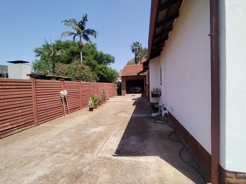 A side view of the property featuring a concrete driveway, timber fencing, and access to a detached garage with a tiled roof.
