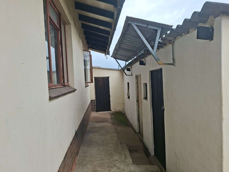 A narrow exterior side passage featuring a concrete walkway, corrugated metal awning, and access doors to the rear of the property.
