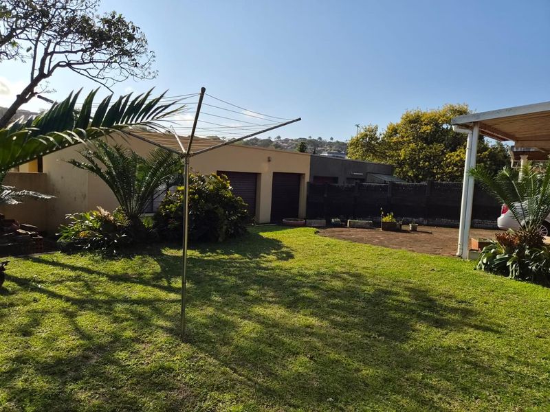 A spacious rear garden featuring a paved patio area, a well-maintained lawn, and access to a double garage.