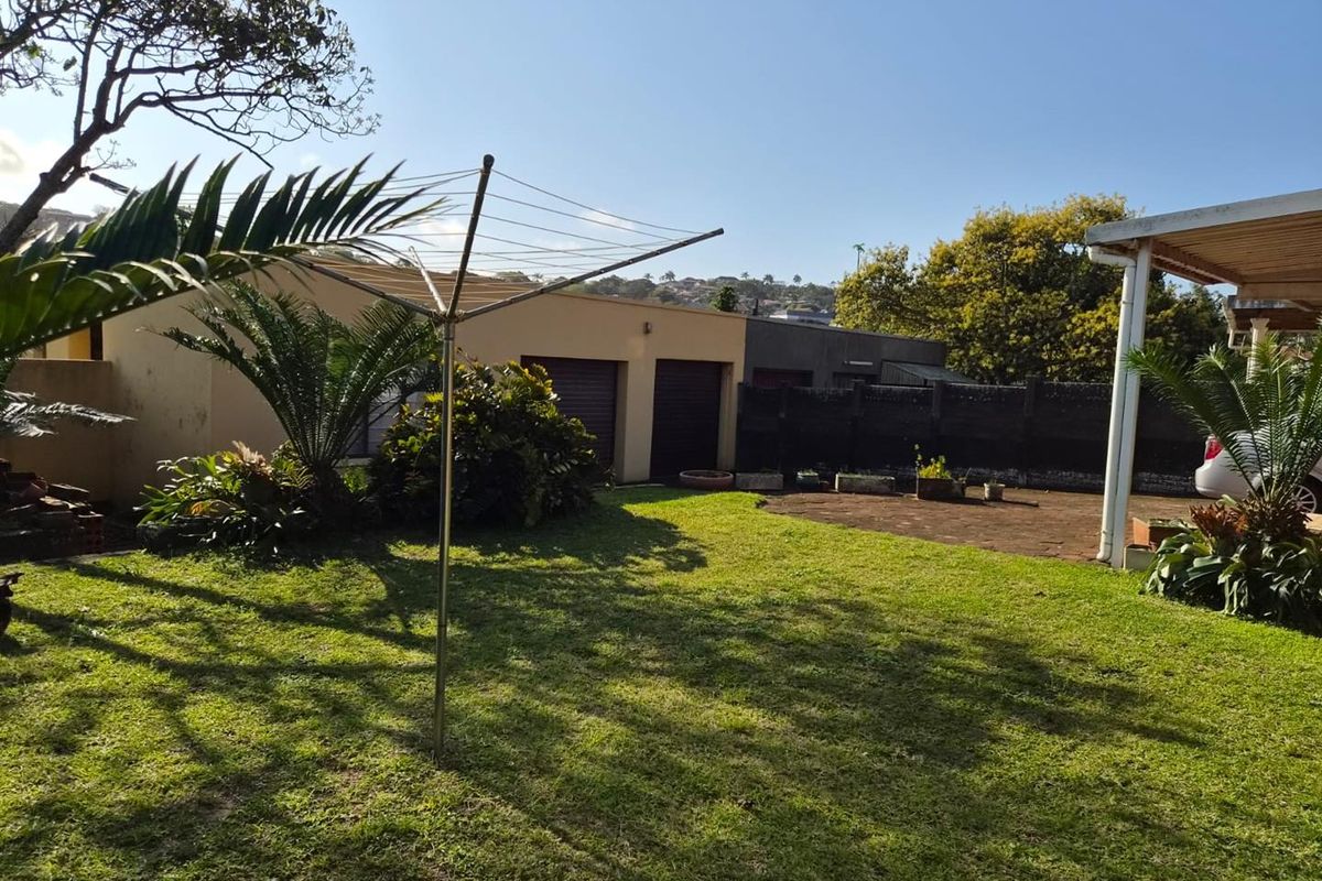 A spacious rear garden featuring a paved patio area, a well-maintained lawn, and access to a double garage.