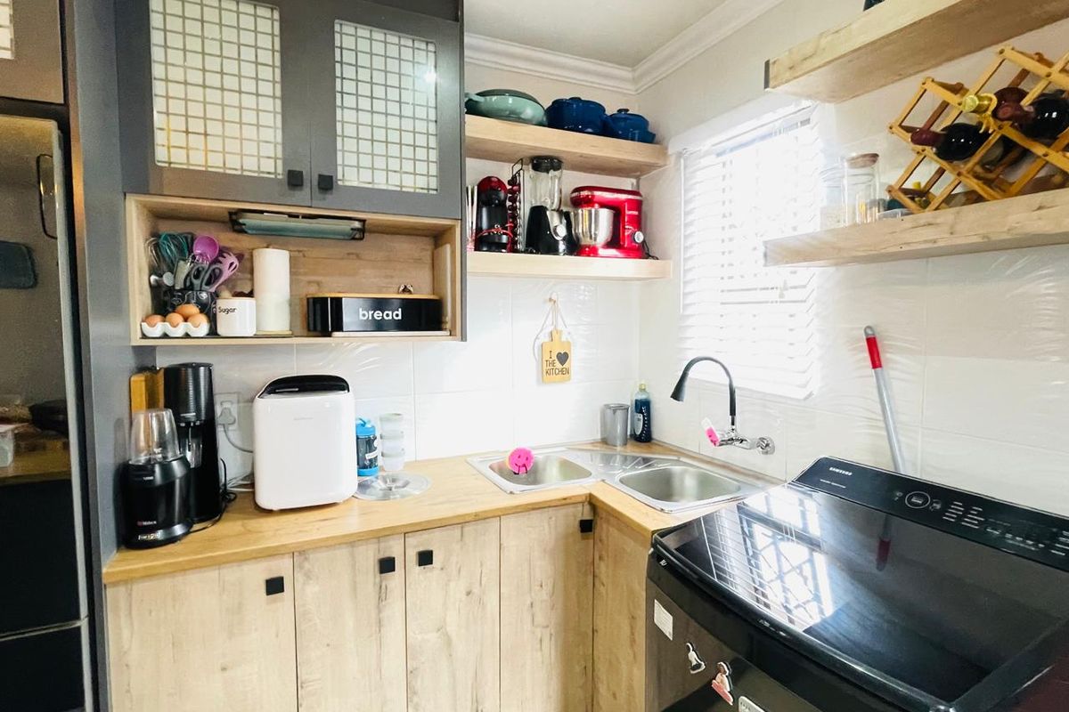 A compact kitchen featuring light wood-look cabinetry, butcher block countertops, a corner stainless steel sink, and open timber shelving.