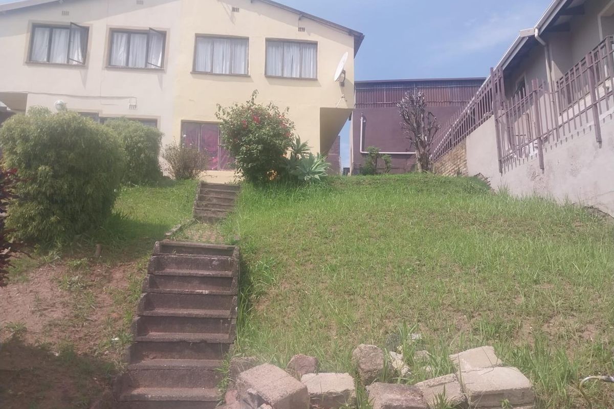 Rear view of the property featuring a sloped garden area with a concrete staircase and metal perimeter fencing.