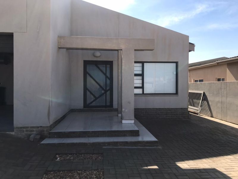 Front entrance of a modern house featuring a tiled porch, contemporary front door, aluminium windows, and a paved driveway.