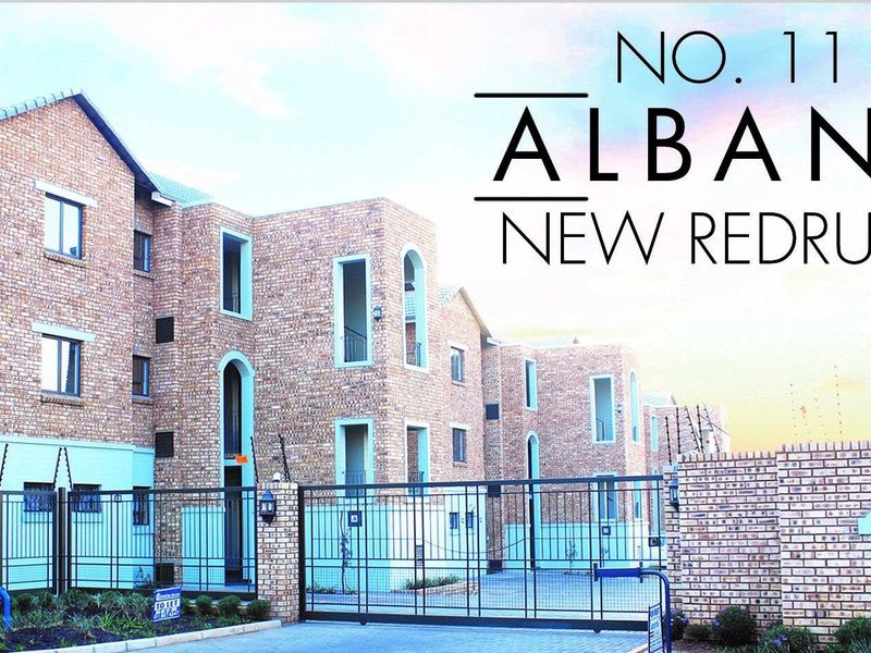 Front elevation of a face brick townhouse complex featuring secure gated access, paved driveway, and perimeter electric fencing.