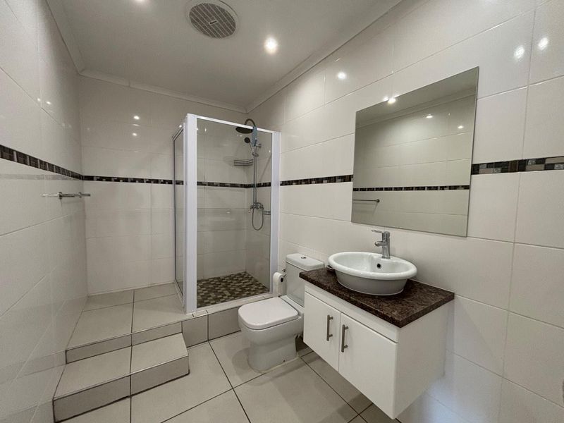 A clean, modern bathroom featuring a glass-enclosed shower, a floating vanity with a vessel sink, and neutral wall tiling.