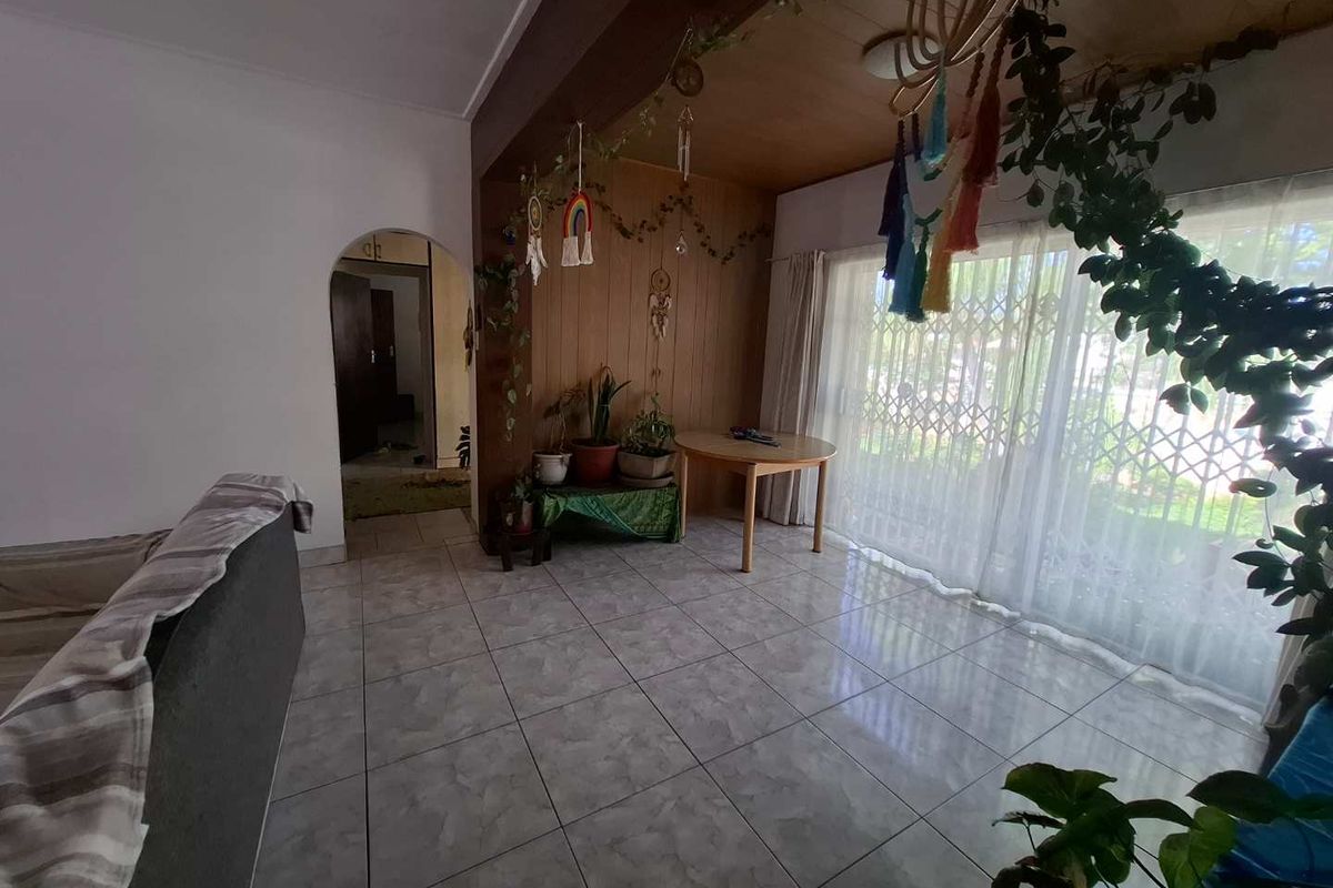 A living area featuring tiled flooring, wood-paneled accent wall, and large sliding glass doors with security gate leading to the exterior.