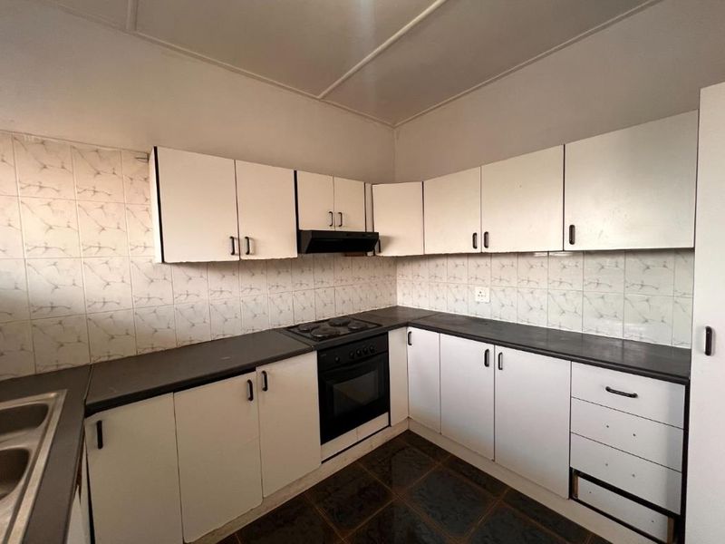 A functional kitchen featuring white built-in cabinetry, dark countertops, an integrated oven and hob, and a tiled backsplash, ready for a modern update.