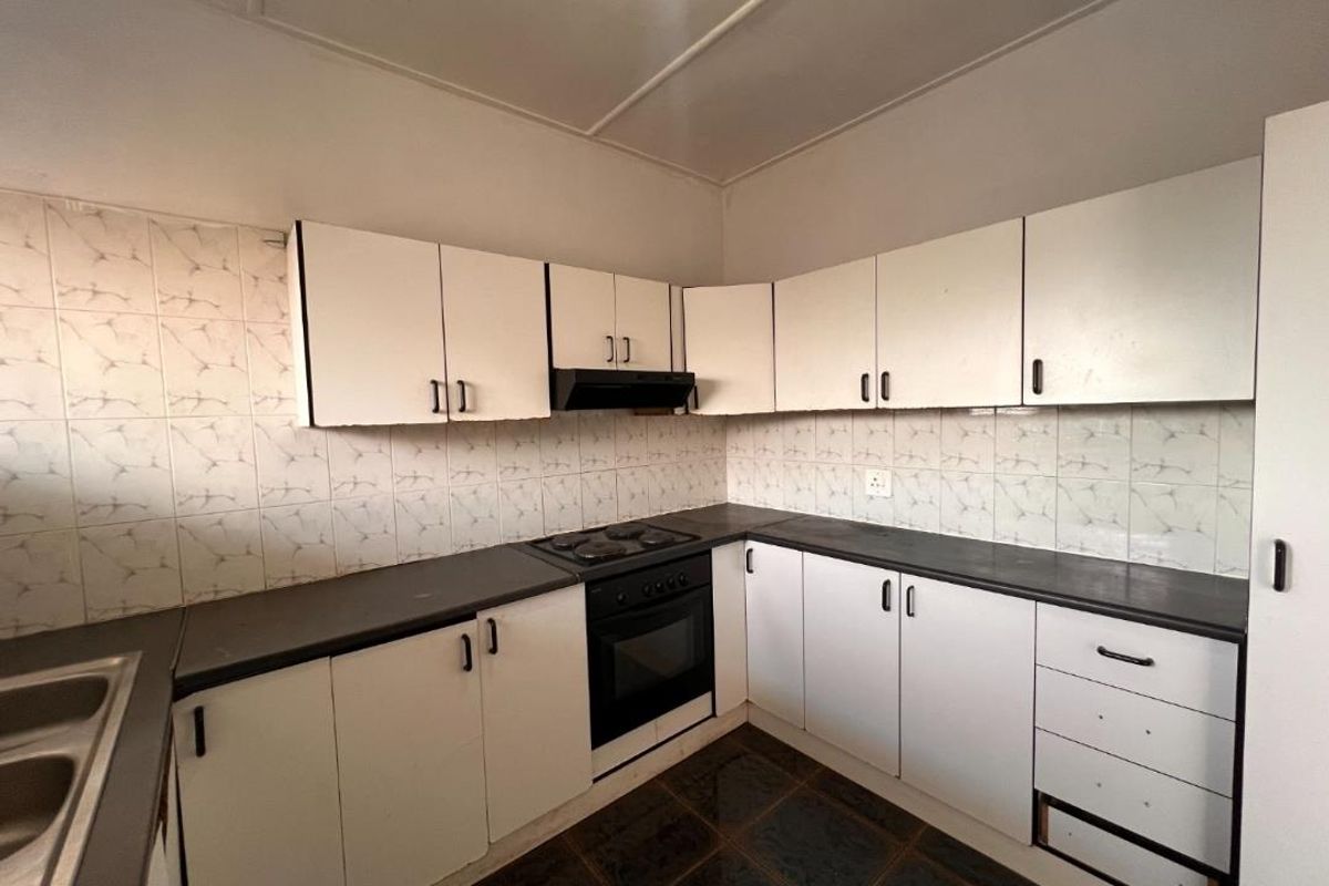 A functional kitchen featuring white built-in cabinetry, dark countertops, an integrated oven and hob, and a tiled backsplash, ready for a modern update.
