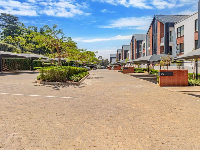 A well-maintained townhouse complex driveway featuring paved surfaces, covered parking bays, and modern brick and glass architectural facades.