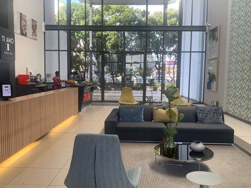 Modern office reception area featuring a large reception desk, high ceilings, and expansive floor-to-ceiling glass windows providing ample natural light.
