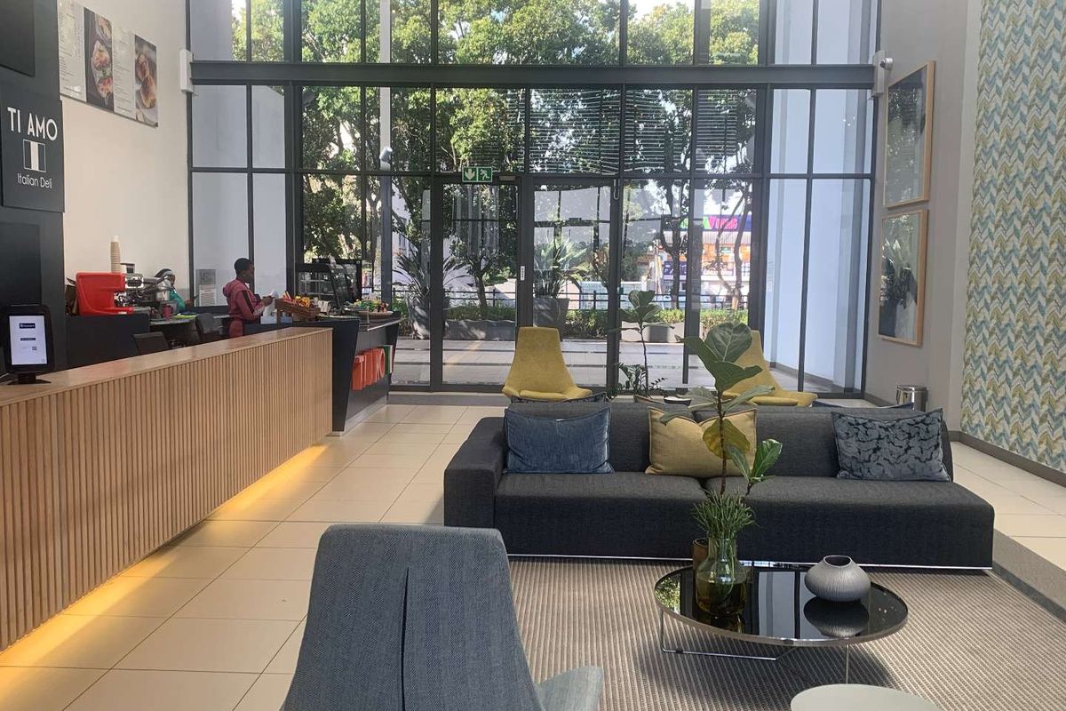 Modern office reception area featuring a large reception desk, high ceilings, and expansive floor-to-ceiling glass windows providing ample natural light.