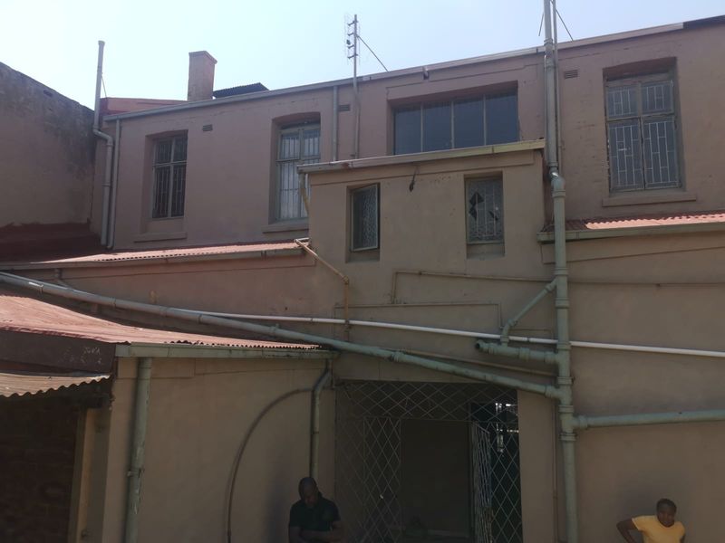 Rear exterior view of the apartment building showing weathered facade, exposed plumbing, security bars, and a broken window pane.