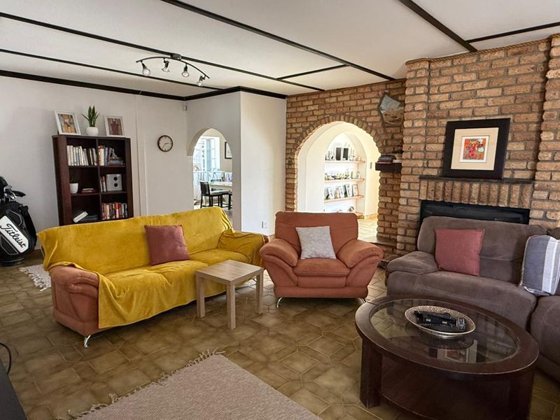 Spacious living room featuring a prominent brick fireplace, exposed beam ceiling, and classic arched doorways leading to adjacent living areas.