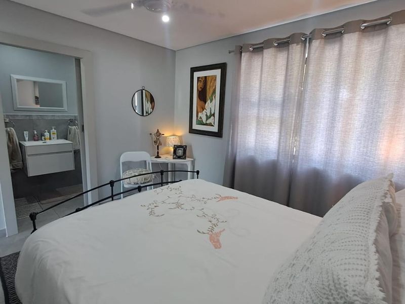 A well-maintained bedroom featuring a ceiling fan, recessed lighting, and an en-suite bathroom with a modern vanity.