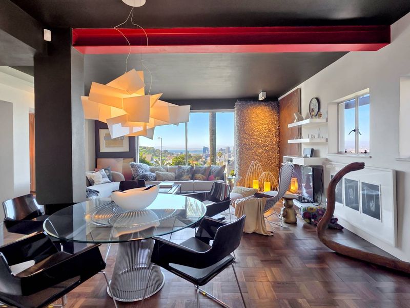 Spacious open-plan living and dining area featuring rich parquet flooring, a striking red exposed steel beam, and expansive windows with city views.