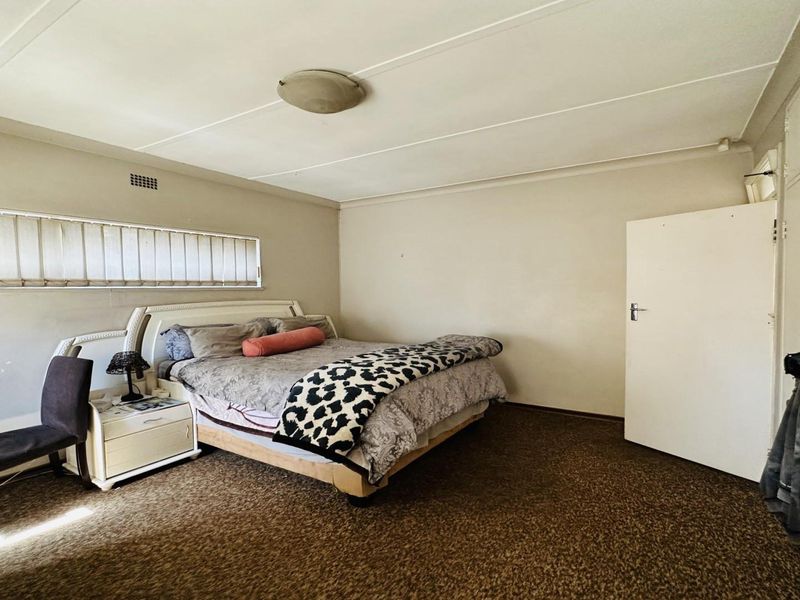 A spacious bedroom featuring built-in cupboards, carpeted flooring, and a horizontal window with blinds, offering a functional layout ready for modernization.