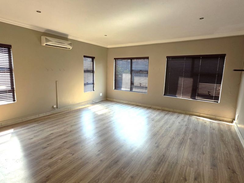 Spacious living room featuring laminate flooring, recessed downlights, venetian blinds, and a wall-mounted split-system air conditioner.