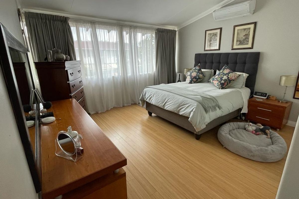 A well-maintained bedroom featuring light-toned laminate flooring and a wall-mounted split-system air conditioning unit.