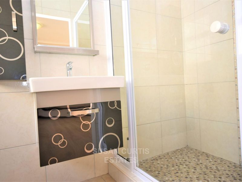 A compact bathroom featuring a wall-mounted vanity with decorative cabinetry, a glass-enclosed shower with mosaic floor tiling, and neutral wall tiles.