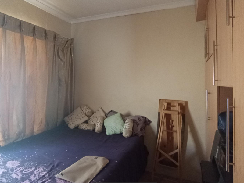 A bedroom featuring built-in wooden cupboards and a window with curtains.