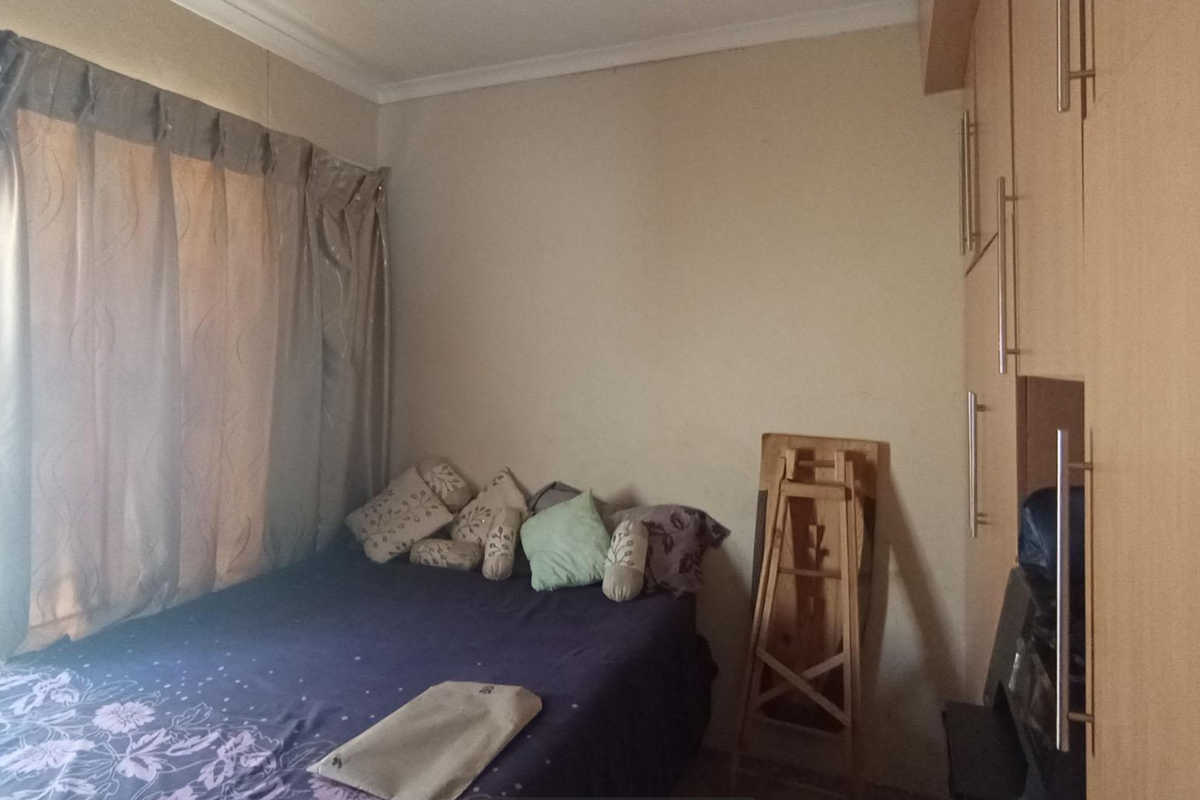 A bedroom featuring built-in wooden cupboards and a window with curtains.