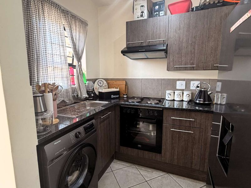 Compact kitchen featuring dark wood cabinetry, granite countertops, built-in oven, electric hob, extractor fan, and integrated space for a washing machine.