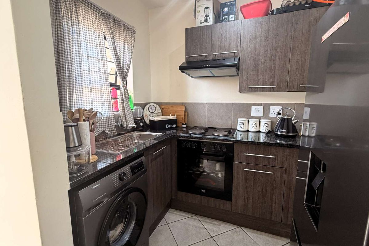 Compact kitchen featuring dark wood cabinetry, granite countertops, built-in oven, electric hob, extractor fan, and integrated space for a washing machine.