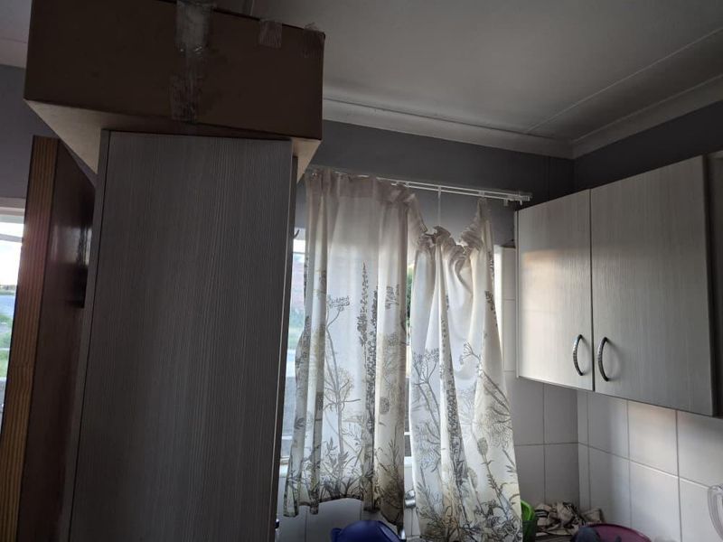 A kitchen area featuring built-in cabinetry and a tiled backsplash, currently showing signs of wear and dated finishes.