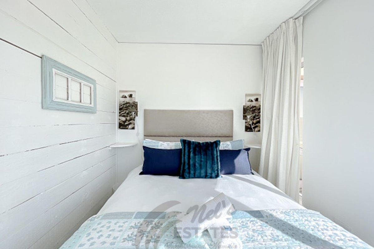 A bright bedroom featuring white horizontal timber wall paneling, a neutral upholstered headboard, and integrated bedside shelving.