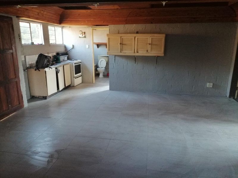Open plan living area featuring tiled floors, timber ceiling, and a basic kitchenette with adjacent bathroom access.