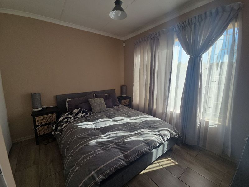 A well-lit bedroom featuring neutral wall tones, tiled flooring, and large windows with curtain treatments, offering a comfortable and functional living space.