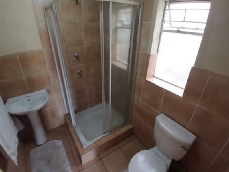 A compact bathroom featuring a pedestal basin, toilet, and a glass-enclosed shower with tiled walls and flooring.