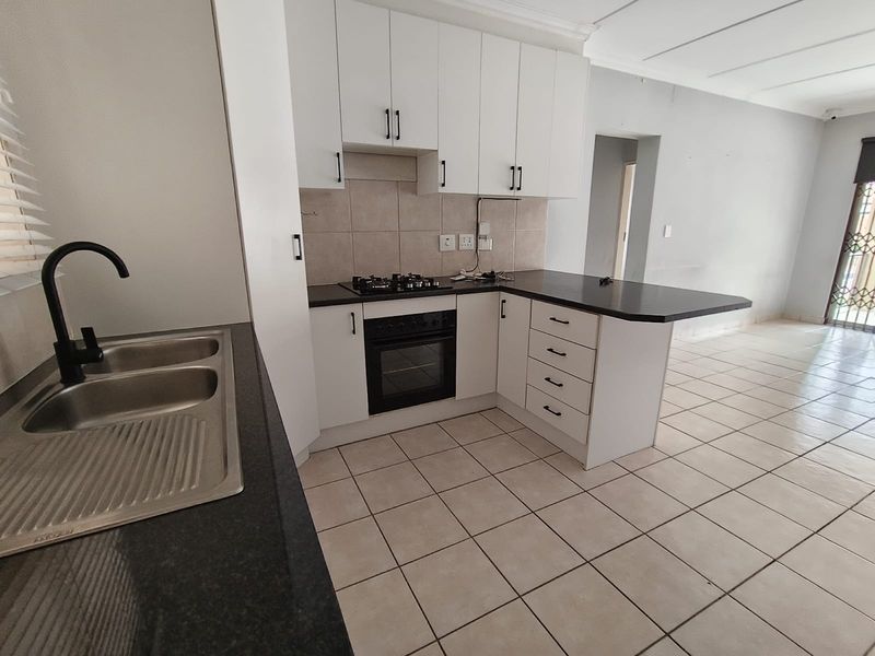 A clean, modern kitchen featuring white cabinetry, dark countertops, a built-in oven with gas hob, and tiled flooring in an open-plan layout.