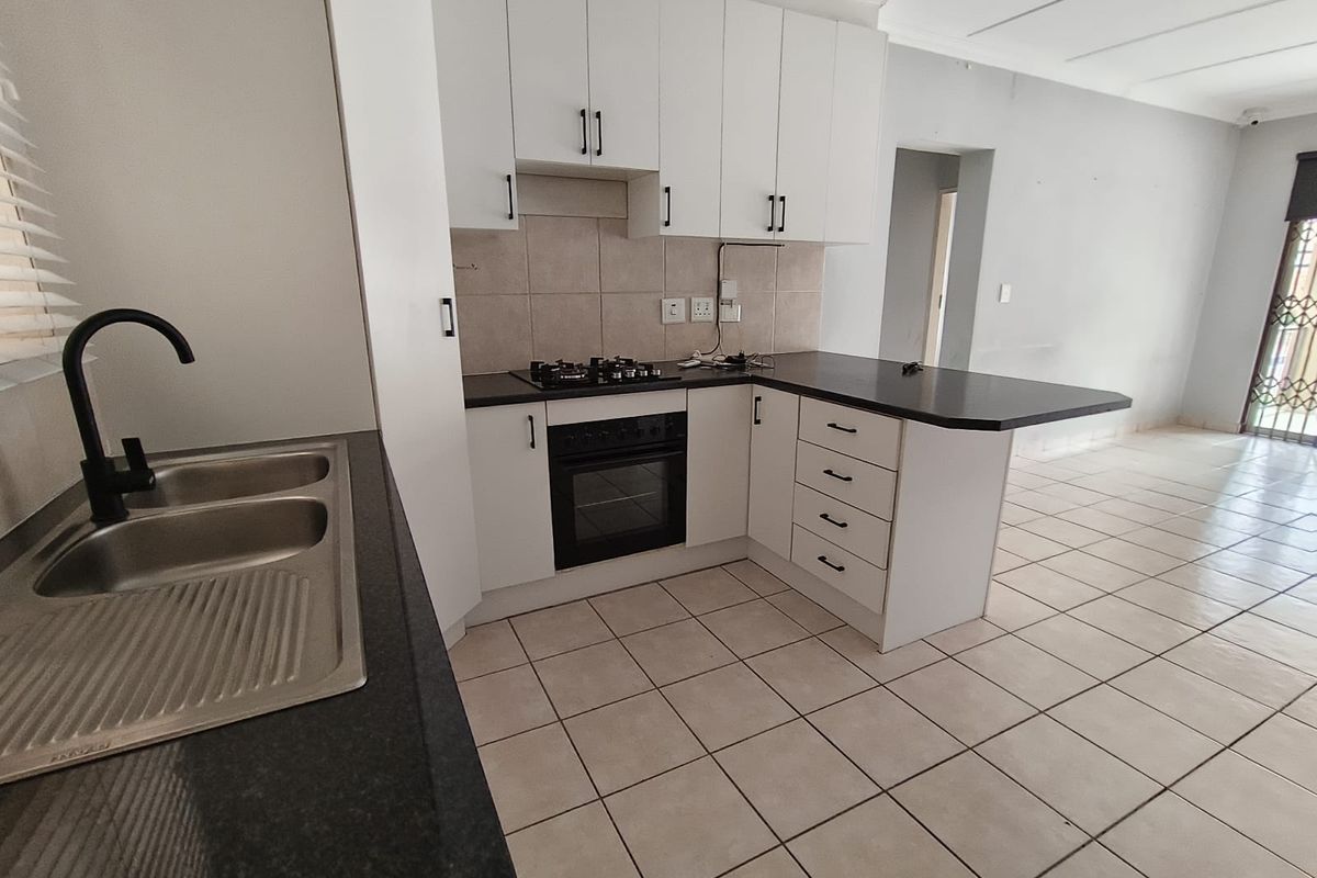 A clean, modern kitchen featuring white cabinetry, dark countertops, a built-in oven with gas hob, and tiled flooring in an open-plan layout.