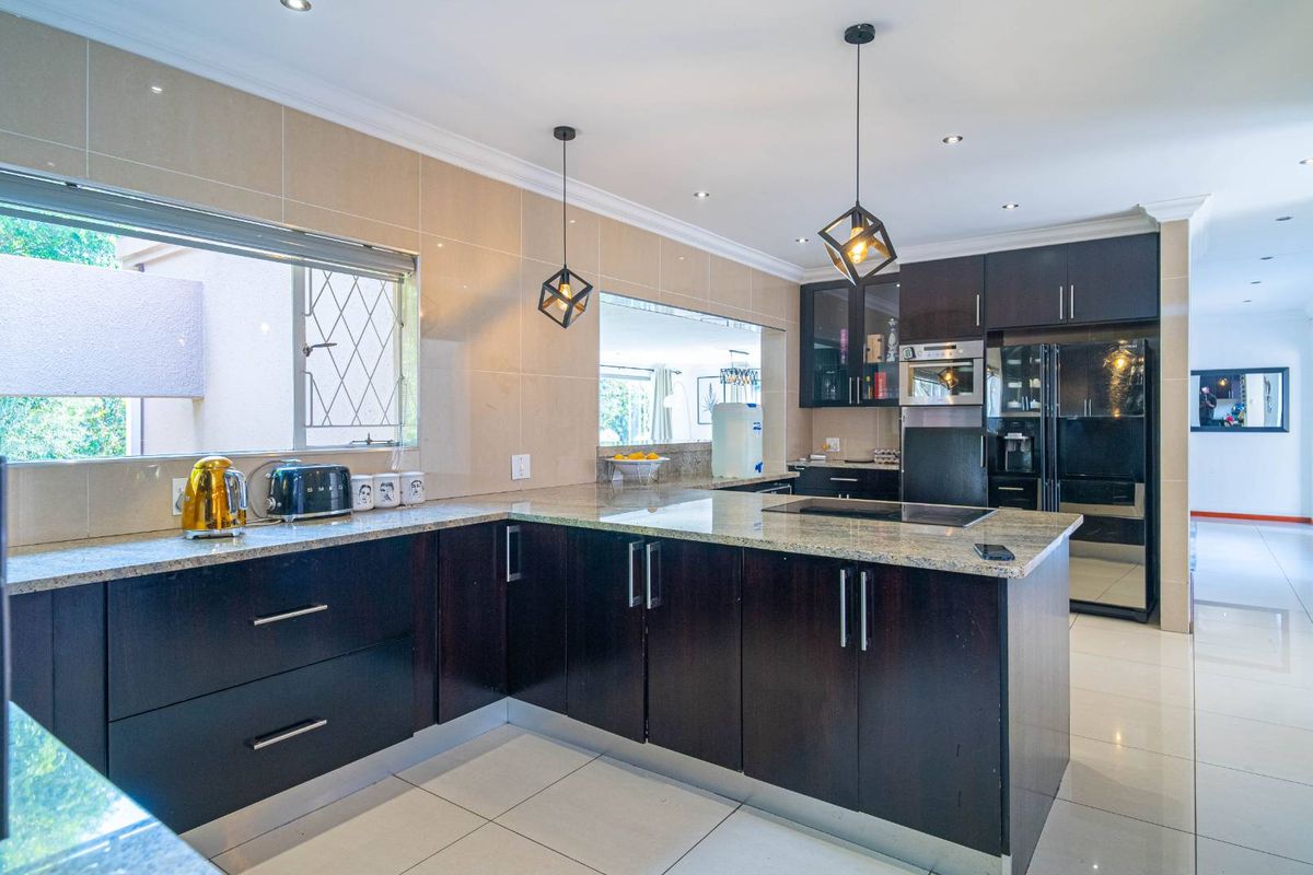 Modern kitchen featuring dark wood cabinetry, granite countertops, integrated appliances, and tiled finishes, offering a clean and functional culinary space.