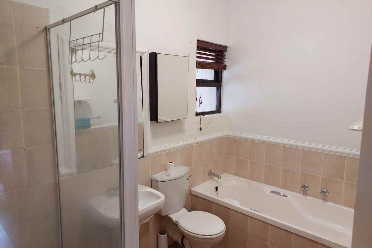 A dated bathroom featuring a built-in bathtub, separate shower enclosure, pedestal basin, and toilet, requiring cosmetic updates to the wall finishes.