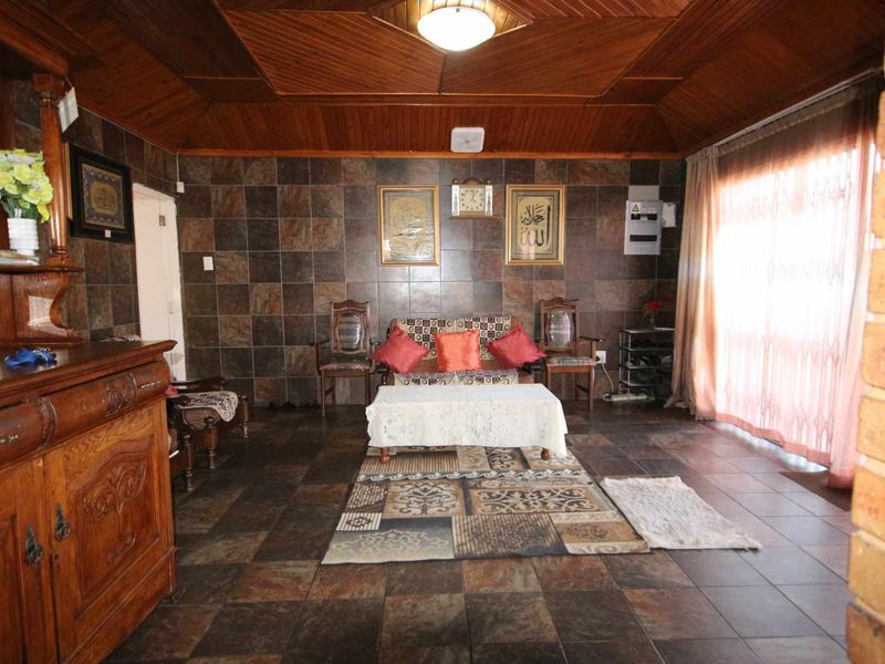 A living room featuring dark tiled walls, timber panelled ceiling, and tiled flooring, with a sliding glass door providing natural light.