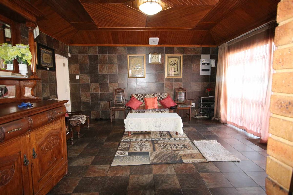 A living room featuring dark tiled walls, timber panelled ceiling, and tiled flooring, with a sliding glass door providing natural light.